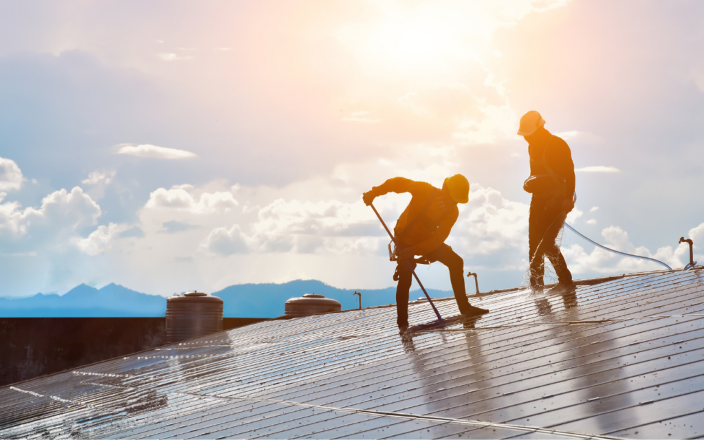 Két férfi a tetőn áll miközben napelem tisztítást hajtanak végbe.